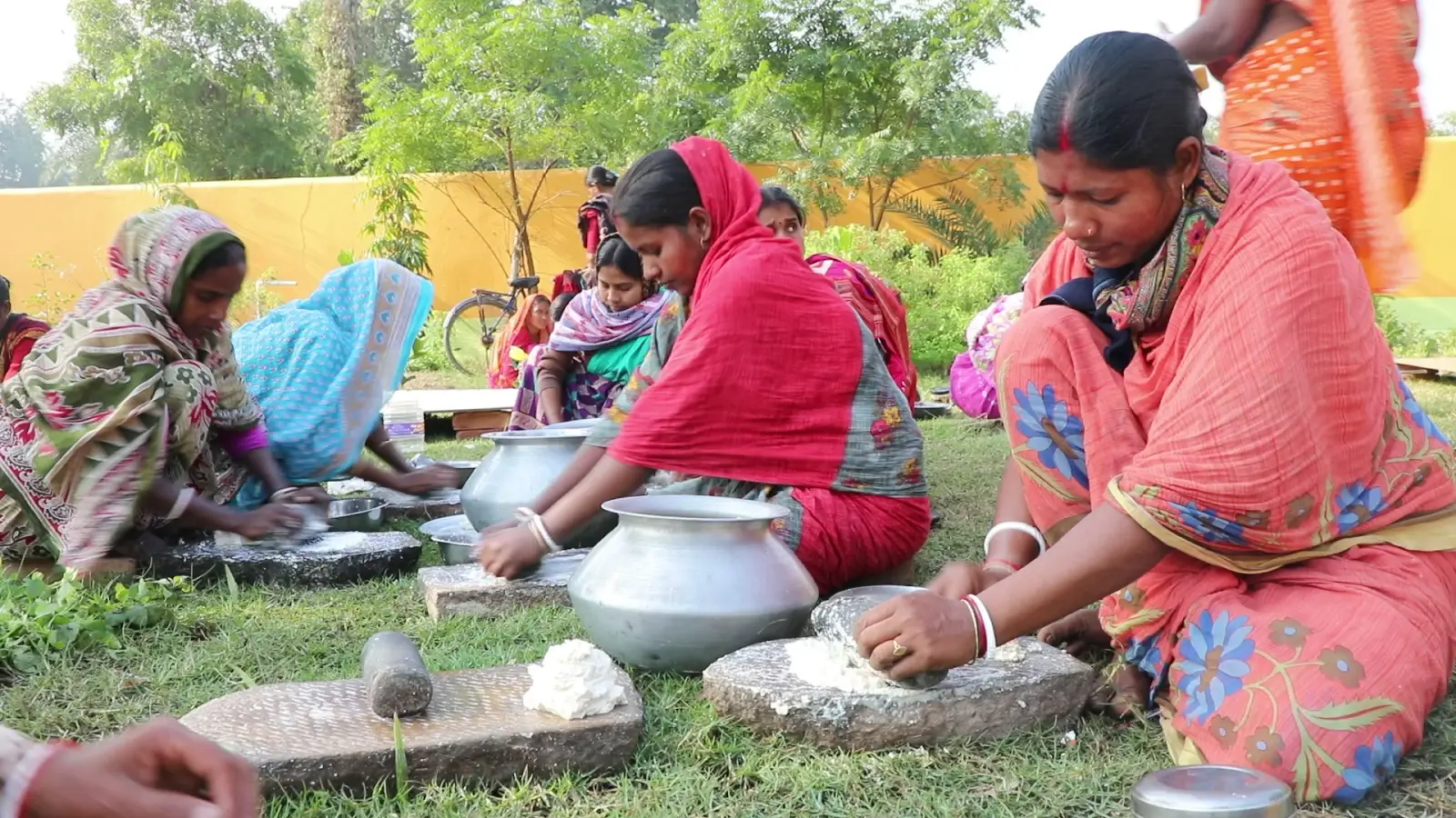 Women grinding soaked lentils on stone slabs in a village garden