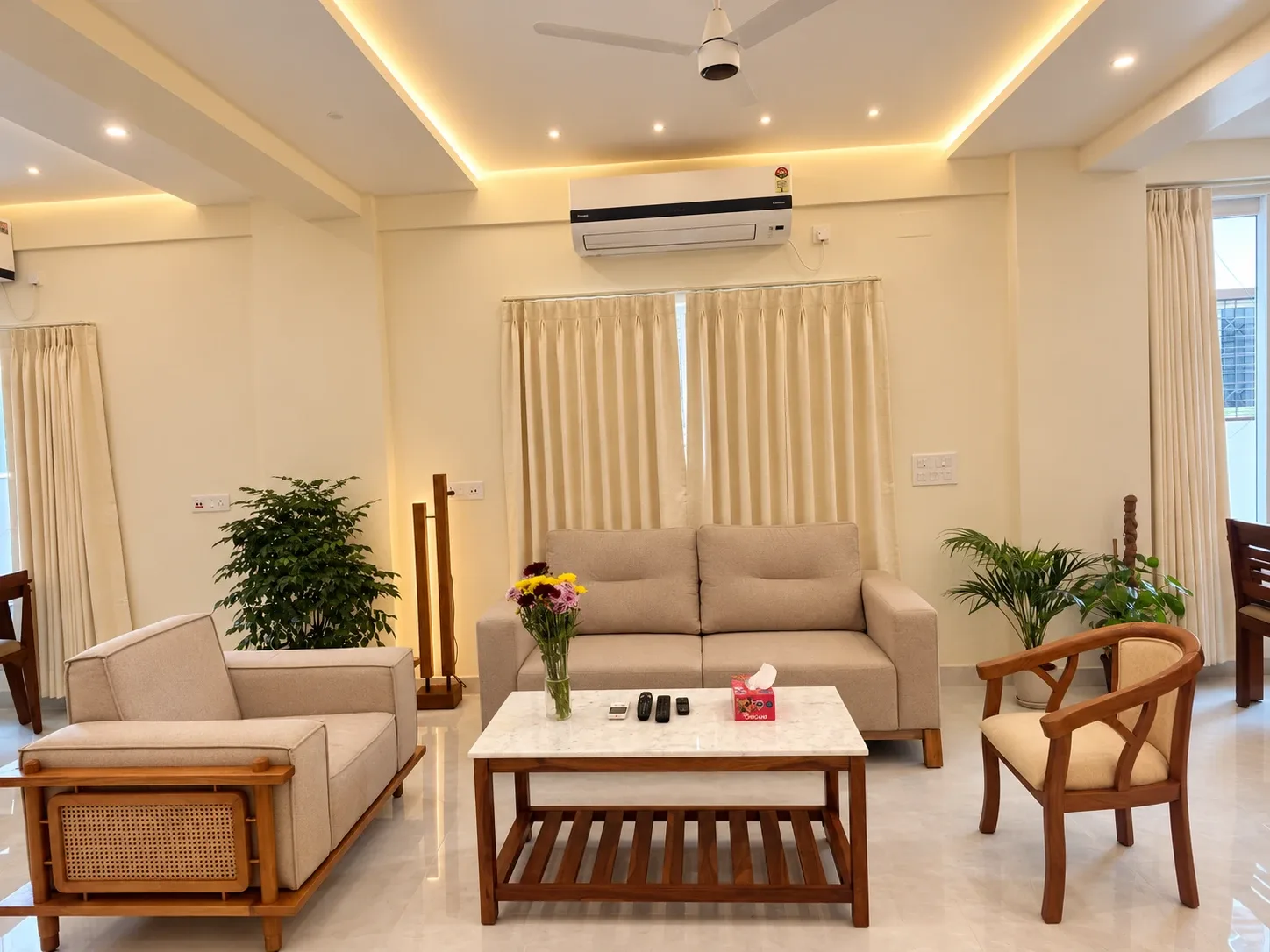 The living room at the Solitude Residency: sofas, a marble coffee table and flowers, in light through cream curtains