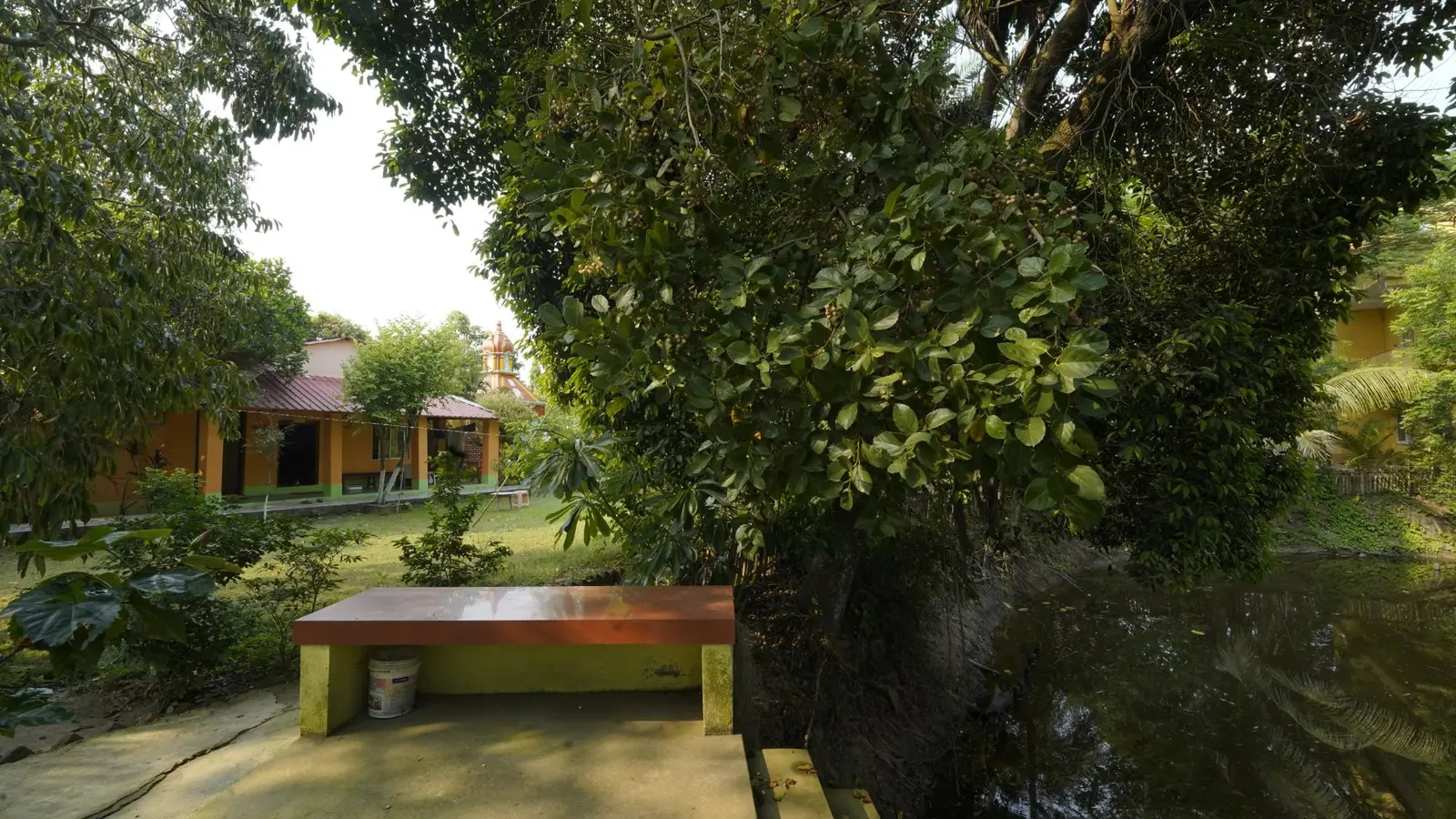 A bench by the pond, with cottages and the temple across the lawn